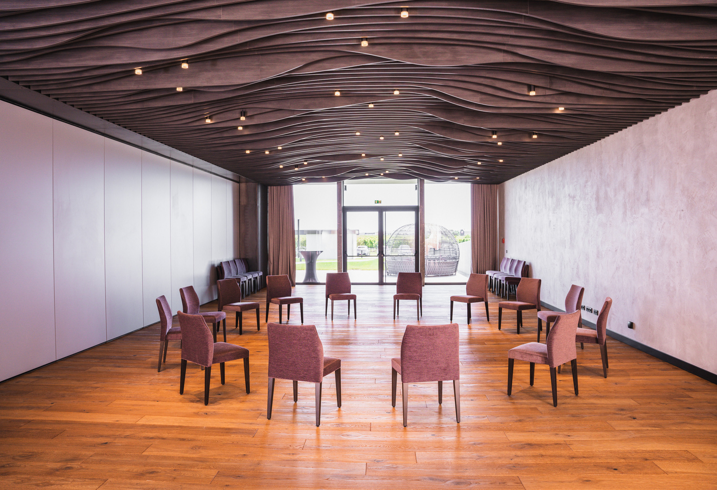 Ein moderner Besprechungsraum mit kreisförmig angeordneten Stühlen, Holzfußboden und einer wellenförmigen Deckengestaltung.