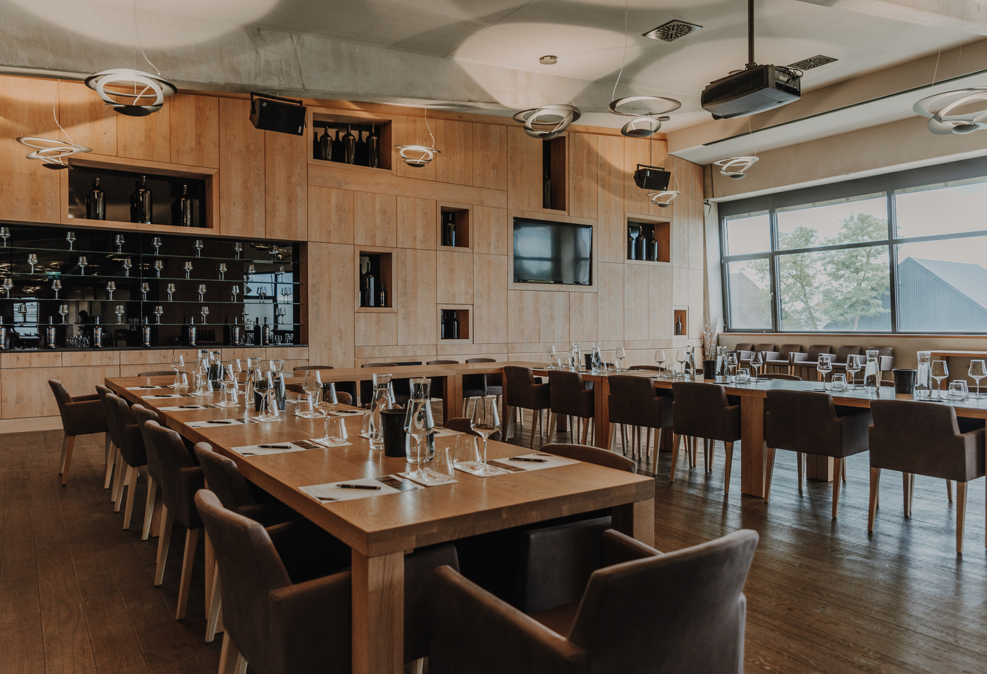 Modernes Restaurant mit Holztischen, braunen Stühlen, Gläser- und Flaschenset, großem Fenster und Wandregalen.