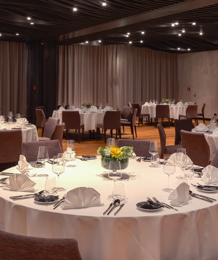 Elegant dining room of a restaurant with round tables set with white linen, glasses and napkins.