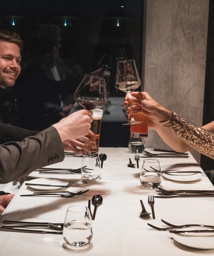Drei Personen stoßen bei einem formellen Abendessen in einem schwach beleuchteten Restaurant über einem weißen Tischtuch an.