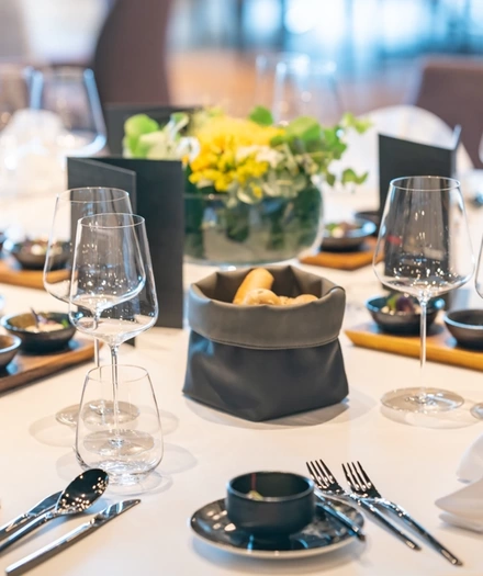 Elegant gedeckter Tisch mit Weingläsern, Besteck, Brotkorb und einem blumengeschmückten Tafelaufsatz auf einem weißen Tischtuch.