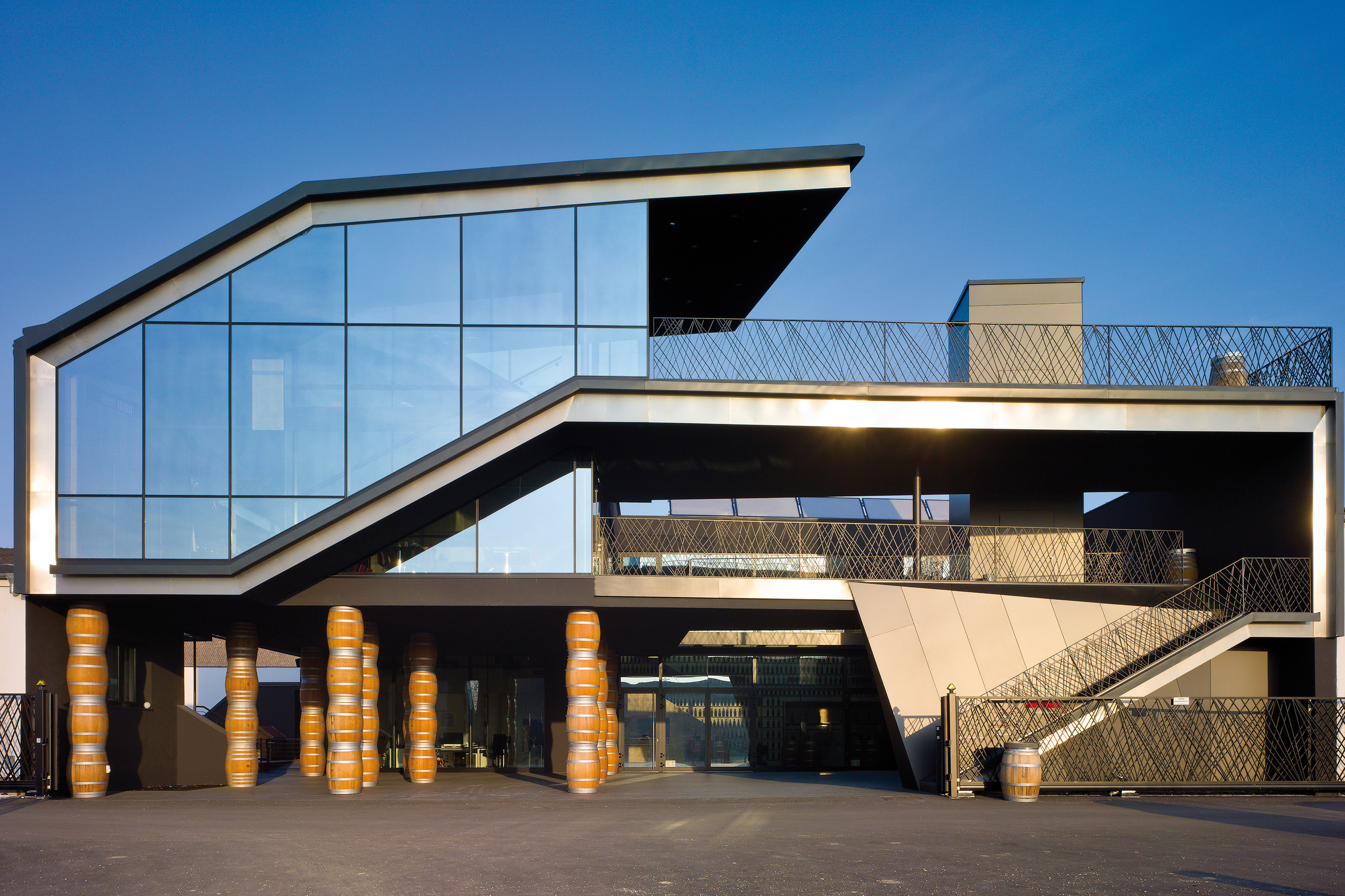 Modernes Gebäude mit großen Glasfenstern, kantigem Design und goldenen Fassdekorationen am Eingang.