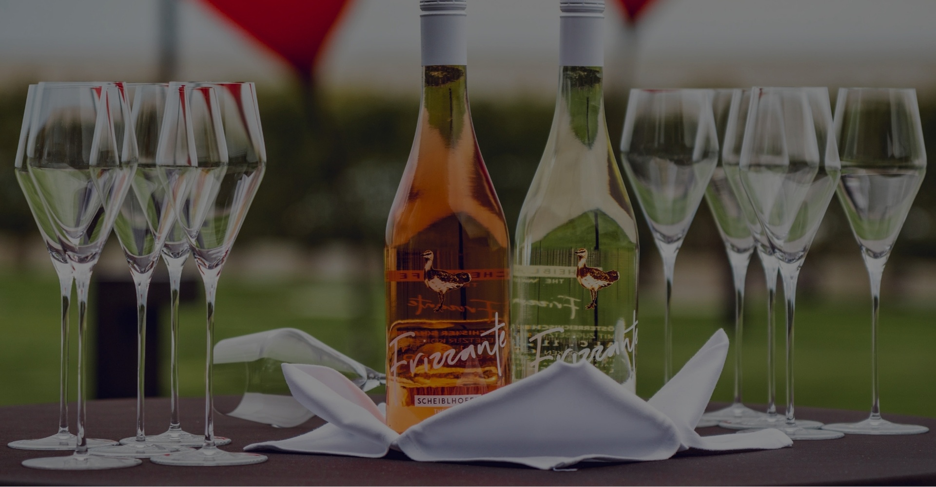 Zwei Weinflaschen und acht leere Weingläser stehen auf einem Tisch mit einer gefalteten weißen Serviette.