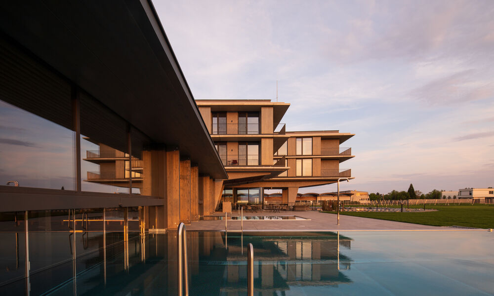 Modernes Hotel mit Holzakzenten und breiten Balkonen, die sich bei Sonnenuntergang in einem blauen Außenpool spiegeln.