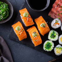 Verschiedene Sushi-Rollen, Seetang-Salat und Sashimi auf einer dunklen Schieferplatte mit einer Schale Sojasauce.