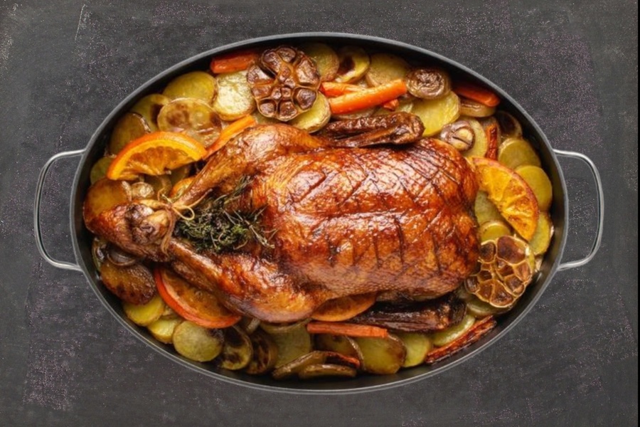 Fry the chicken with herbs, potatoes, carrots, orange slices and garlic in a black frying pan.