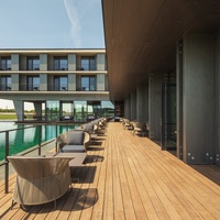 Modern hotel terrace with wooden decking, outdoor seating and views of the building and the water feature.